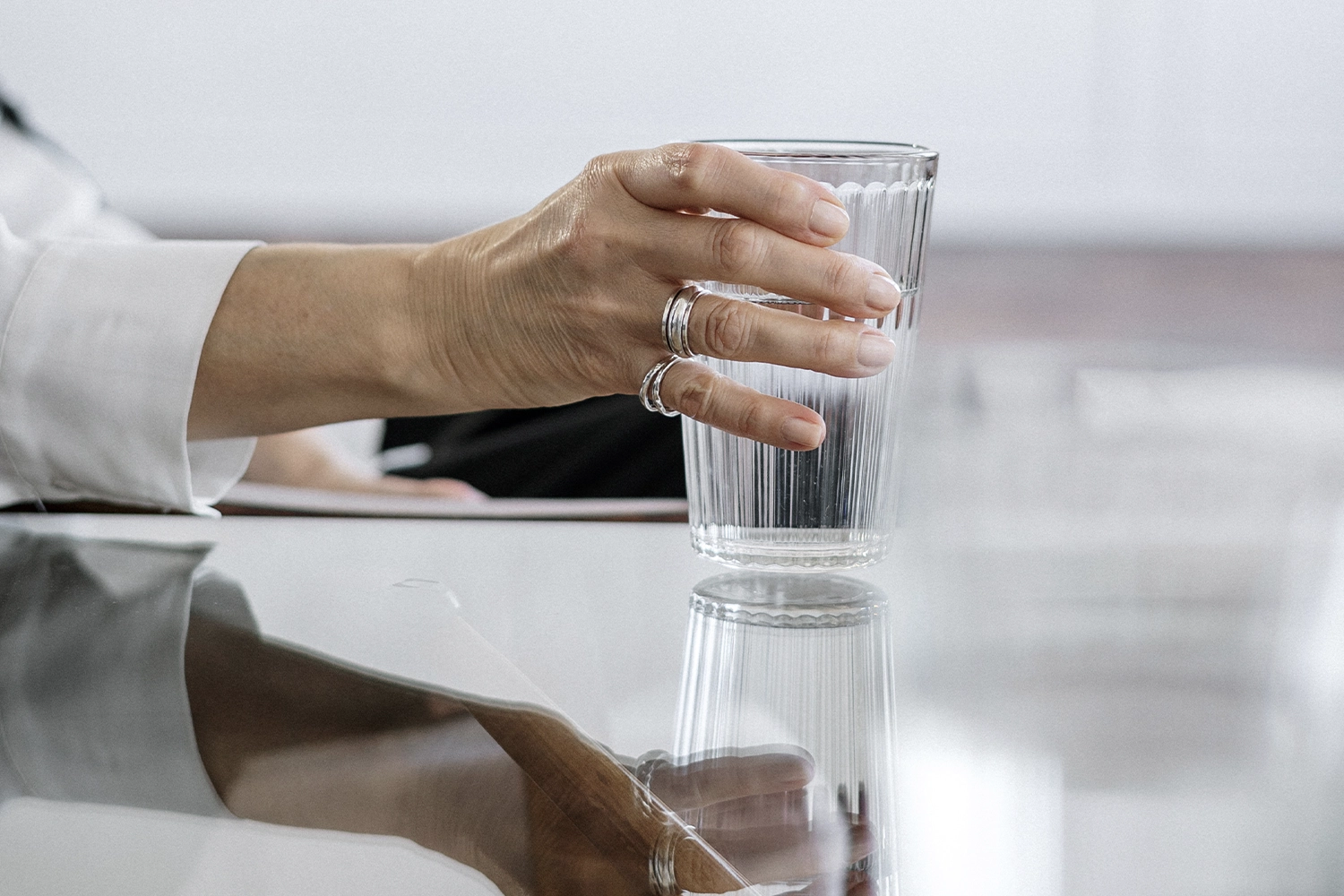 person lifting a glass of water off a glass surface